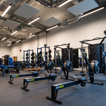 The gym at the fitness centre with a set of rowing machines in the foreground and a set of squat racks in the background